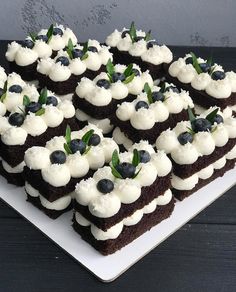 there are many square cakes with white frosting and blue berries on top, sitting on a plate