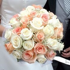 a bride and groom holding a bouquet of white and peach roses with baby's breath