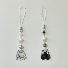 two silver earrings with cats and pearls hanging from the earwires on a white background