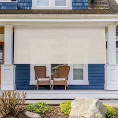 two chairs sitting on the front porch of a blue and white house with an awning