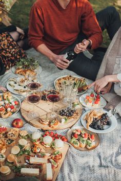 people sitting around a table full of food and drinks, with one person holding a wine bottle