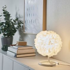 a white lamp sitting on top of a table next to some books and a potted plant