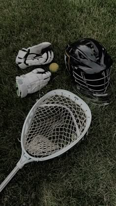 a lacrosse goalie's helmet, glove and ball on the grass next to it