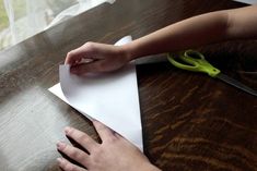 a person cutting paper on top of a wooden table