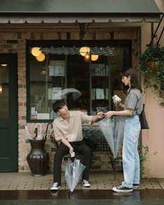 two people sitting on a bench in front of a store with an umbrella over their heads