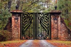 an iron gate is open on a brick path in front of trees and bushes with red leaves