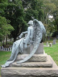 a statue of a woman sitting on top of a stone slab in a cemetery with trees behind it