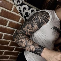 a man with a flower tattoo on his arm and arms is standing in front of a brick wall