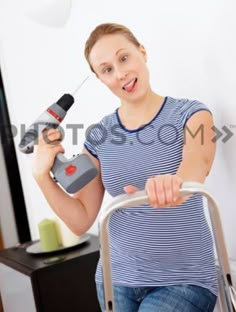 a woman in blue shirt holding a cordless driller and pointing at the camera