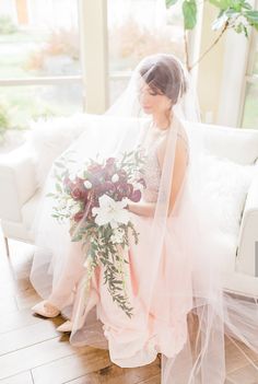 a bride sitting on a couch with her bouquet in hand and veil over her head