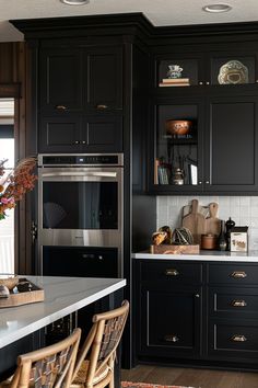 a kitchen with black cabinets and white counter tops, an oven in the center is surrounded by wicker chairs