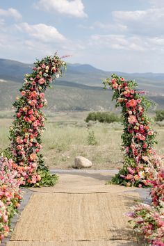 an outdoor wedding ceremony with flowers and greenery on the aisle, in front of mountains