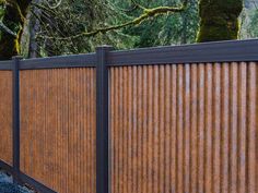 a skateboarder doing a trick on the side of a wooden fence with trees in the background