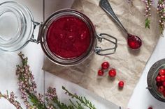 cranberry sauce in a glass jar with spoons and flowers on the side