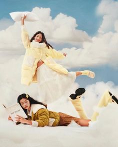 two women are laying in the clouds and one is holding a pillow while the other holds a book