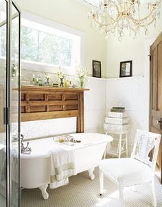 a white bath tub sitting under a chandelier next to a wooden cabinet in a bathroom