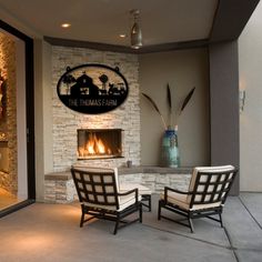 two chairs sitting in front of a fireplace with a clock on the wall above it