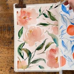 a person is painting flowers on a piece of paper with watercolors and paintbrushes