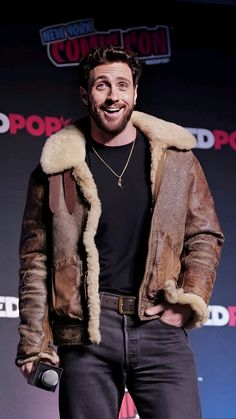 a man standing in front of a microphone wearing a brown jacket and fur lined collar