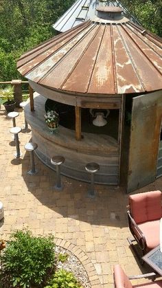 an outdoor kitchen made out of a round metal structure with stools and tables around it