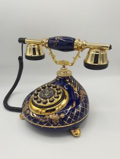 an old fashioned blue and gold phone with two bells on the top, sitting on a white surface