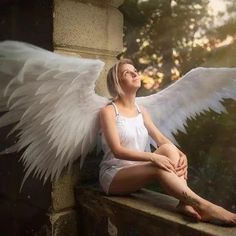 a woman with white wings sitting on a ledge