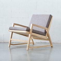 a wooden chair sitting in front of a white brick wall with grey fabric on it