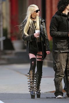 a woman with long blonde hair wearing black boots and holding a cup in her hand