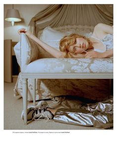 a woman laying on top of a bed next to a white table with a lamp