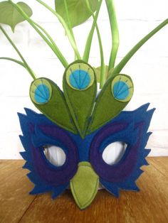 a blue and green mask sitting on top of a wooden table next to a plant