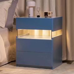 a night stand with an alarm clock on it next to a bed