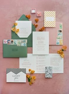 the wedding stationery is laid out on a pink surface with yellow flowers and green envelopes