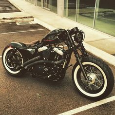 a black motorcycle parked in a parking lot next to a glass building with lots of windows