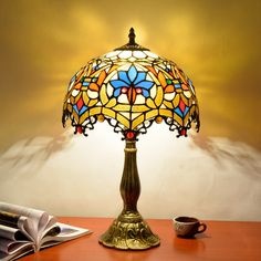 a table lamp sitting on top of a wooden desk next to a book and cup