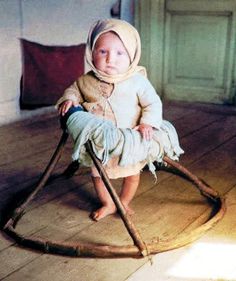 a small child sitting on top of a wooden rocking chair with a blanket over it's head