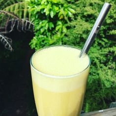 a glass with a straw in it sitting on a table next to some bushes and trees