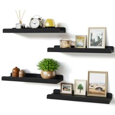 two black floating shelves with pictures and frames on them, one has a potted plant