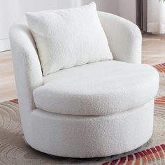 a white chair with pillows on top of it in a living room next to a rug