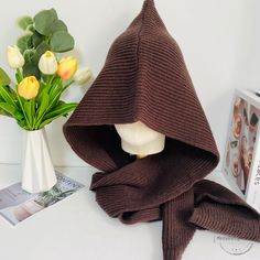 a brown knitted hooded scarf next to a vase with tulips