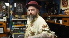 a man with tattoos and a hat sitting in a room full of shelves filled with items