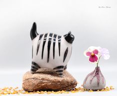 a zebra figurine sitting on top of a rock next to a vase filled with flowers