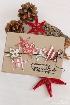 a christmas card with paper stars and pine cones on the top, along with twine ribbons