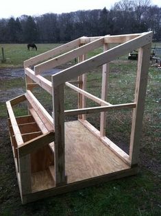 an unfinished dog house built in the middle of a field with a horse grazing behind it