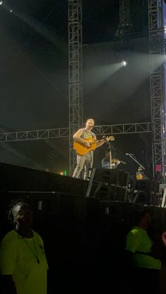 a man standing on top of a stage with a guitar in his hand and people around him