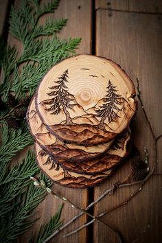 three wooden coasters with pine trees on them sitting next to evergreen needles and branches