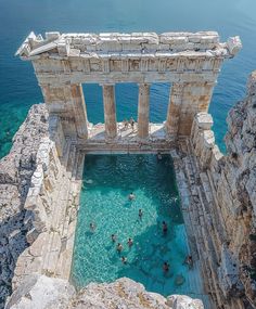 people are swimming in the blue water near an ancient structure