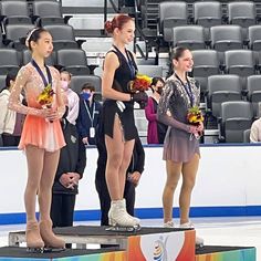 two women standing on a podium with flowers in their hands and one woman wearing an ice skating outfit