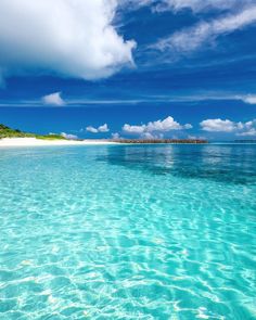 the water is very clear and blue with some clouds in the sky above it,