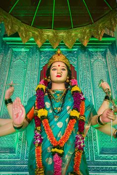 a statue of the hindu god in front of a green wall with gold trimmings