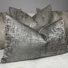 two silver pillows sitting on top of a bed